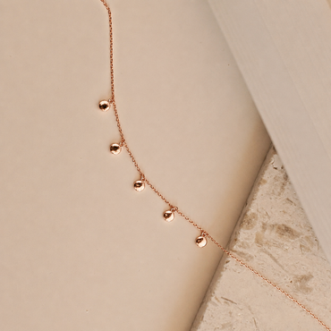 Rose gold necklace with heart-shaped pendants on a beige background
