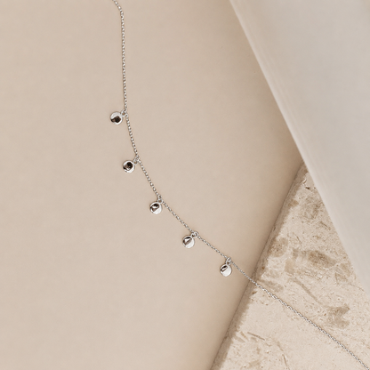 Silver necklace with small round pendants on a beige surface