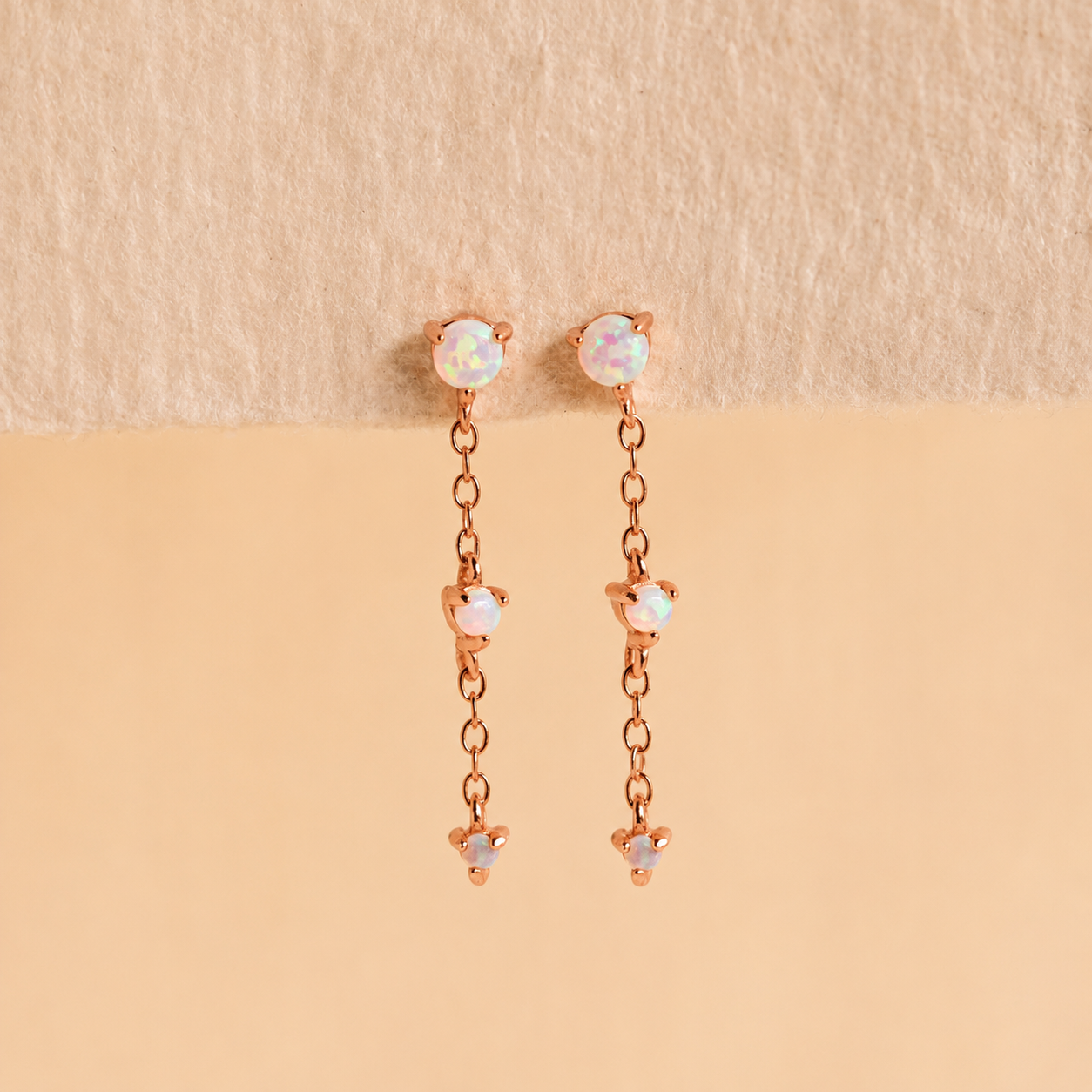 Rose gold earrings with opal stones on a beige background