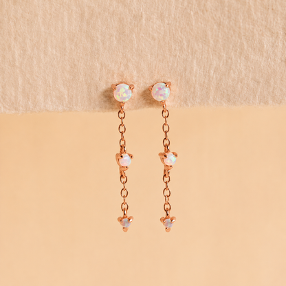 Rose gold earrings with opal stones on a beige background