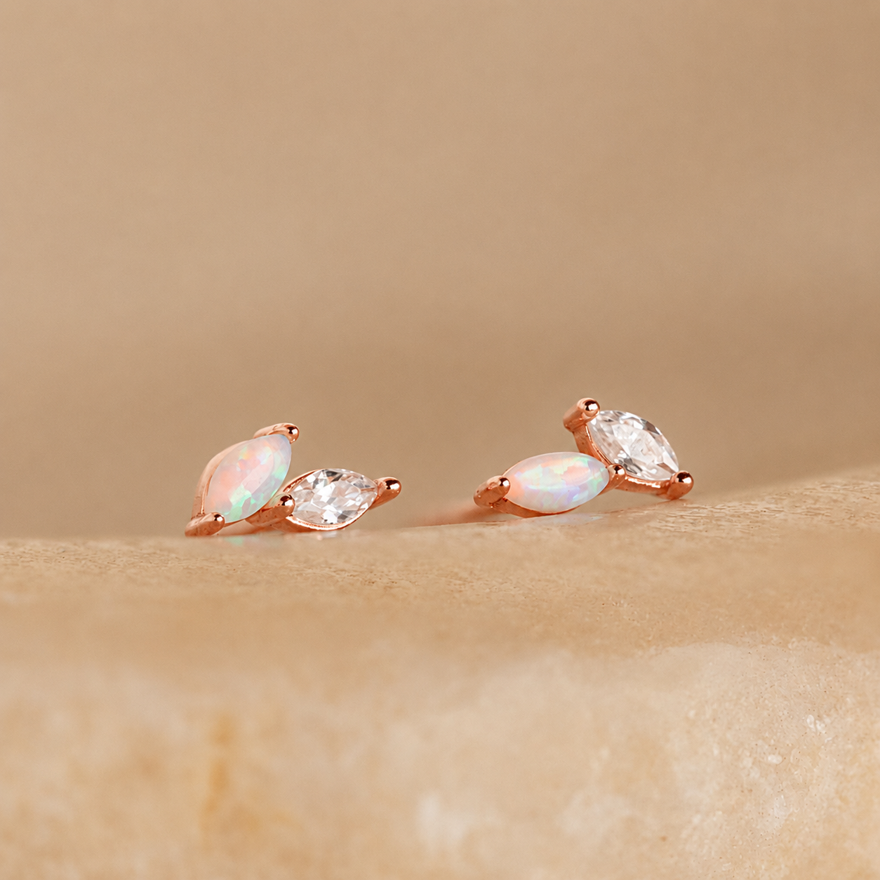 Pair of rose gold earrings with opal and clear gemstones on a beige background