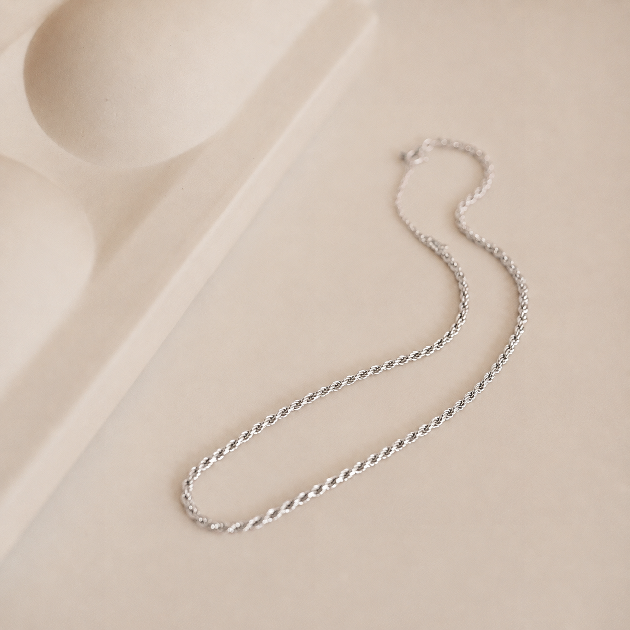 Silver chain necklace on a beige fabric background