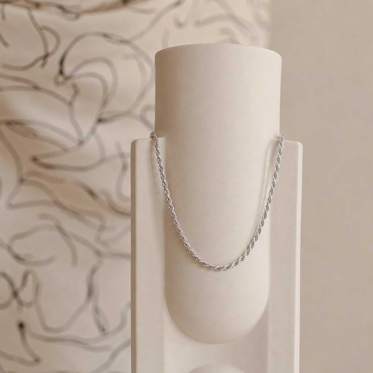 Silver chain necklace on a white cylindrical stand with a neutral background