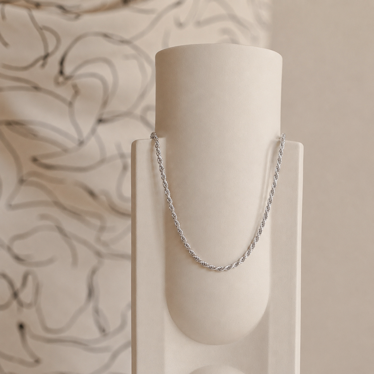 Silver chain necklace on a white cylindrical stand with a neutral background