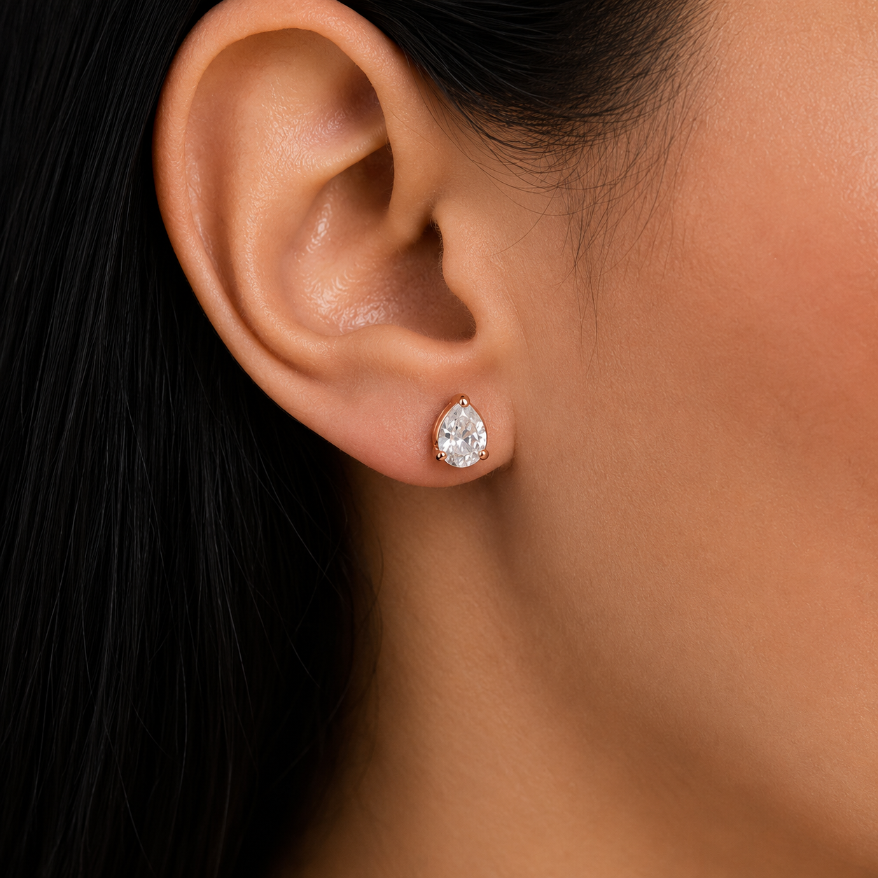 A close-up of a model's ear wearing a small pear-cut diamond stud earring in a silver setting.