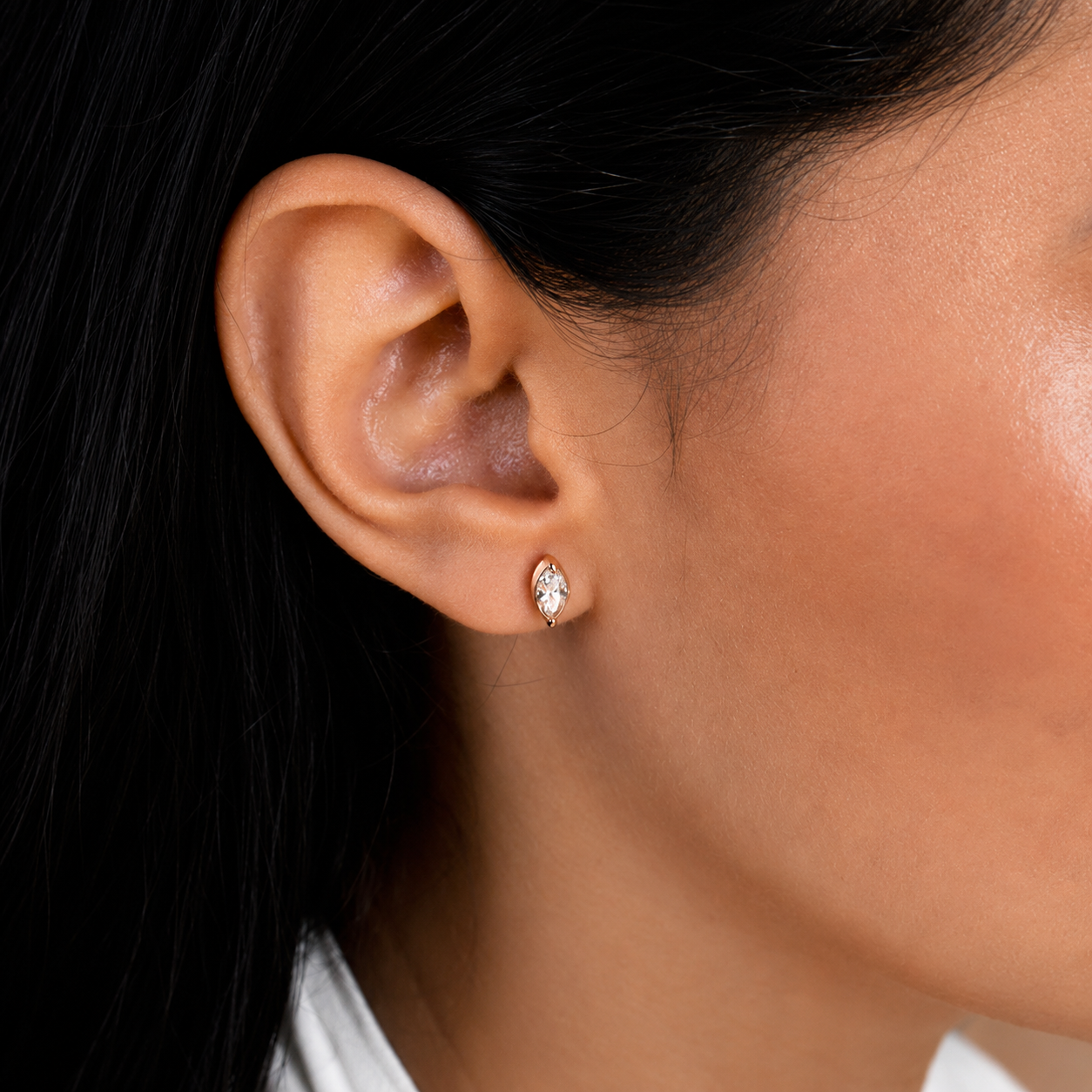 A close-up of a person's ear wearing a small marquise-cut diamond stud earring in a silver setting.