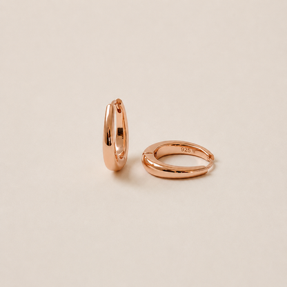 Two slim rose gold hoop earrings shown on a warm beige background, one standing vertically and the other lying horizontally. The horizontal hoop has a small '925' sterling silver purity stamp engraved on the inside.