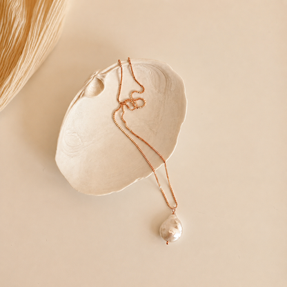Pearl necklace with a pendant on a beige shell against a beige background