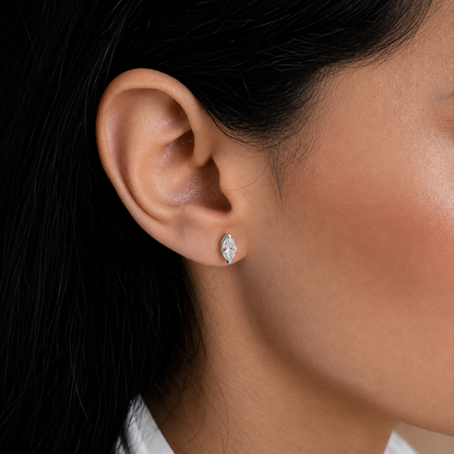 A close-up of a person's ear wearing a small marquise-shaped stud earring with a clear gemstone in a silver-toned setting.