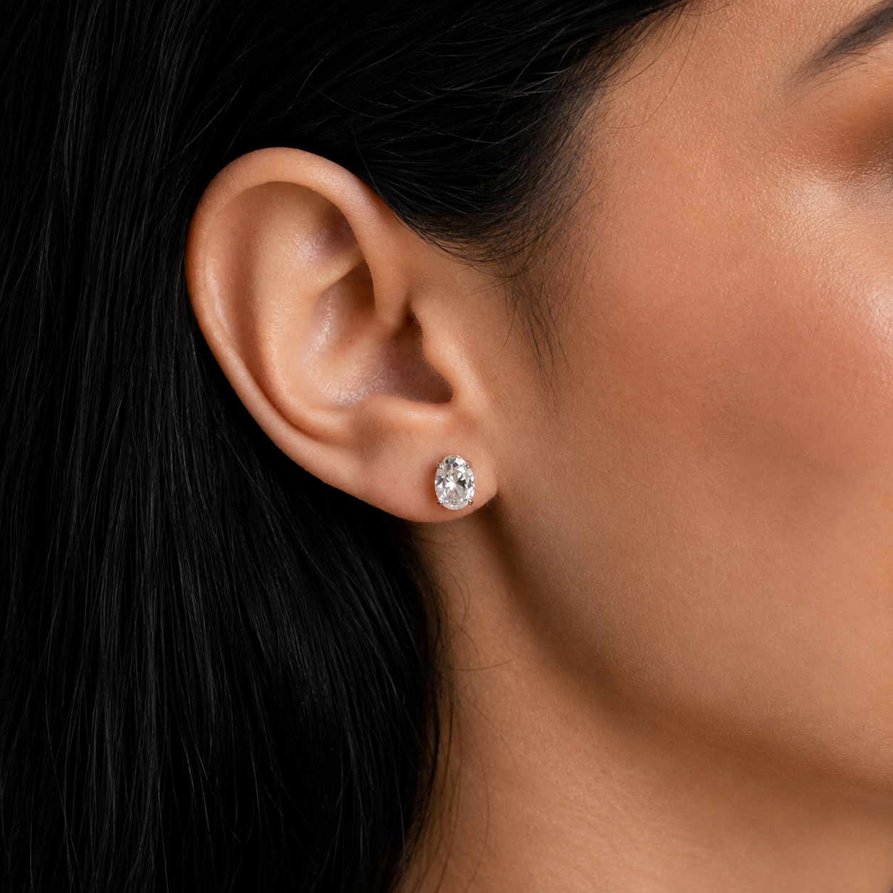 A close-up of a woman's ear wearing a small round clear gemstone stud earring in a silver-toned setting.