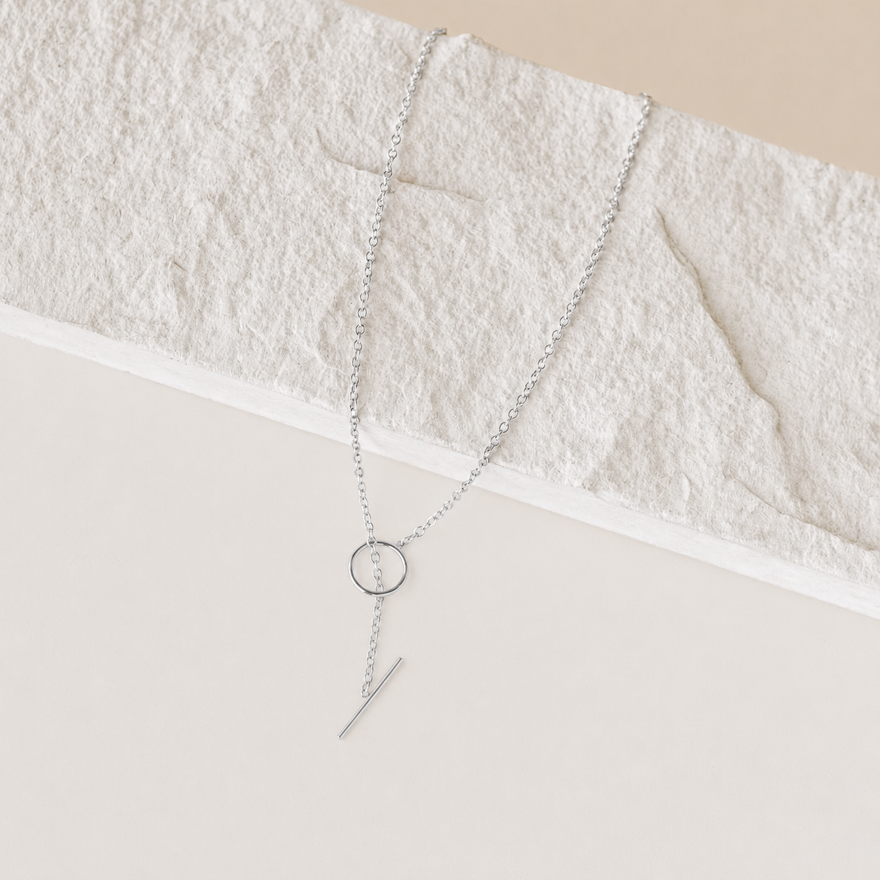 Silver necklace with a circular pendant and a bar on a textured beige surface