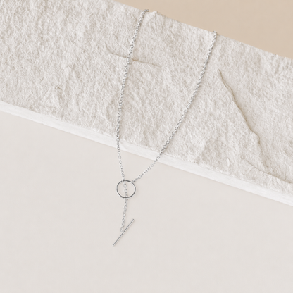 Silver necklace with a circular pendant and a bar on a textured beige surface