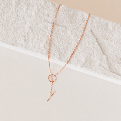 Rose gold necklace with circular and bar pendant on a textured white surface
