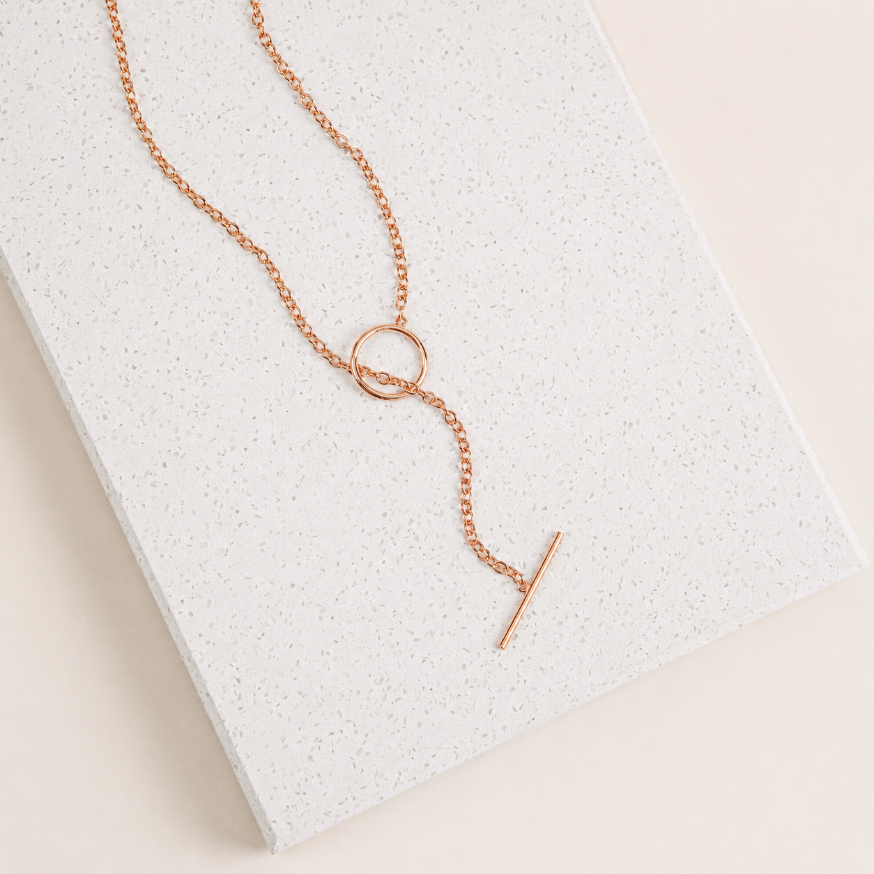 Rose gold necklace with a unique pendant on a textured white surface
