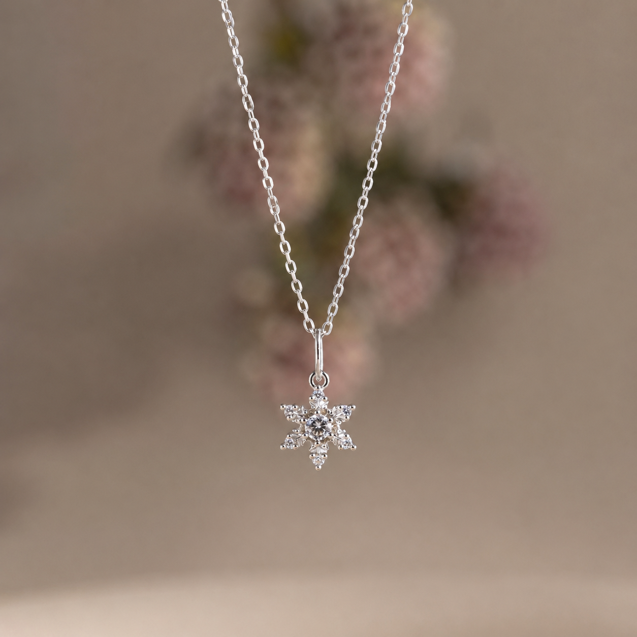 Silver snowflake pendant necklace on a blurred floral background