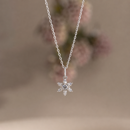 Silver snowflake pendant necklace on a blurred floral background