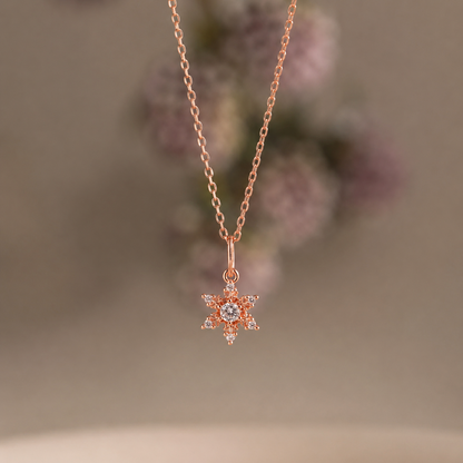 Rose gold necklace with a snowflake pendant on a blurred floral background