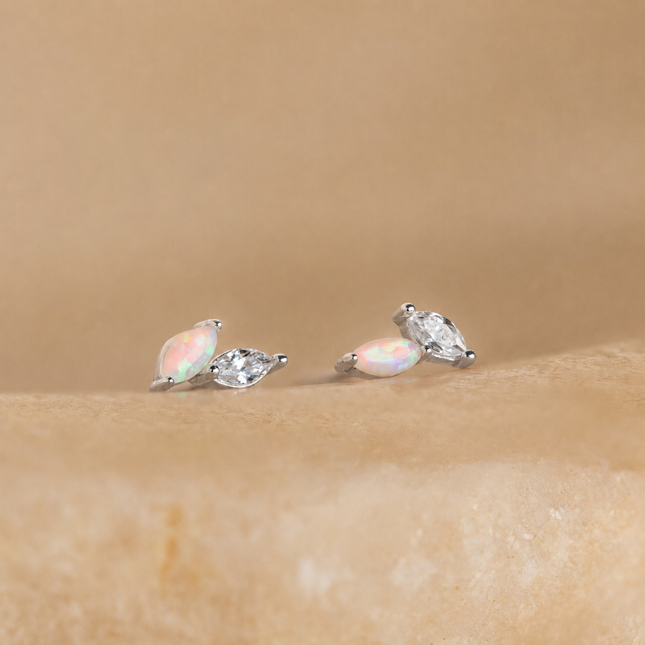 Pair of opal and silver stud earrings on a beige background