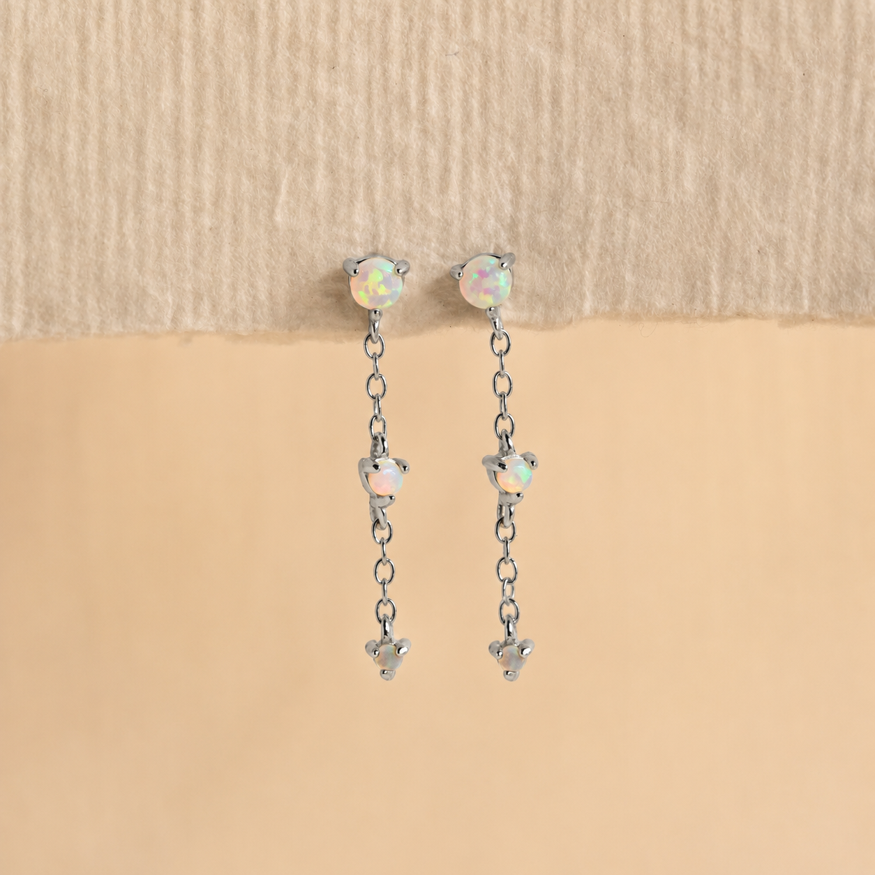 Pair of silver earrings with opal stones on a beige background
