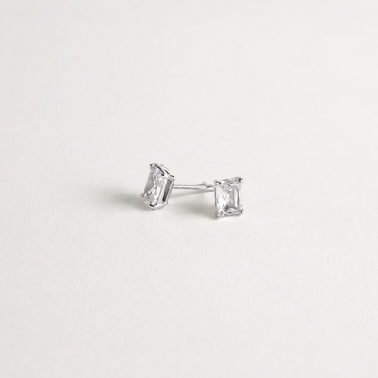 A pair of silver stud earrings with rectangular clear gemstones, displayed on a clean, light off-white background.
