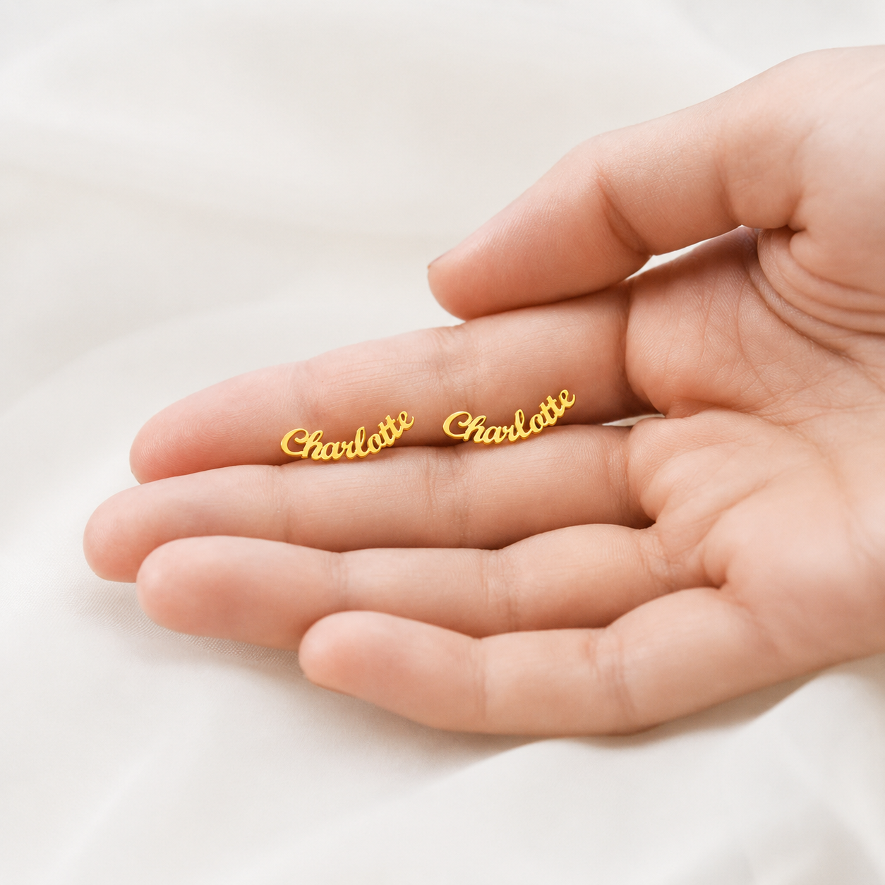 Gold 'Charlotte' earrings on a hand against a white background