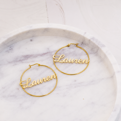 Gold hoop earrings with 'Lauren' engraving on a marble surface