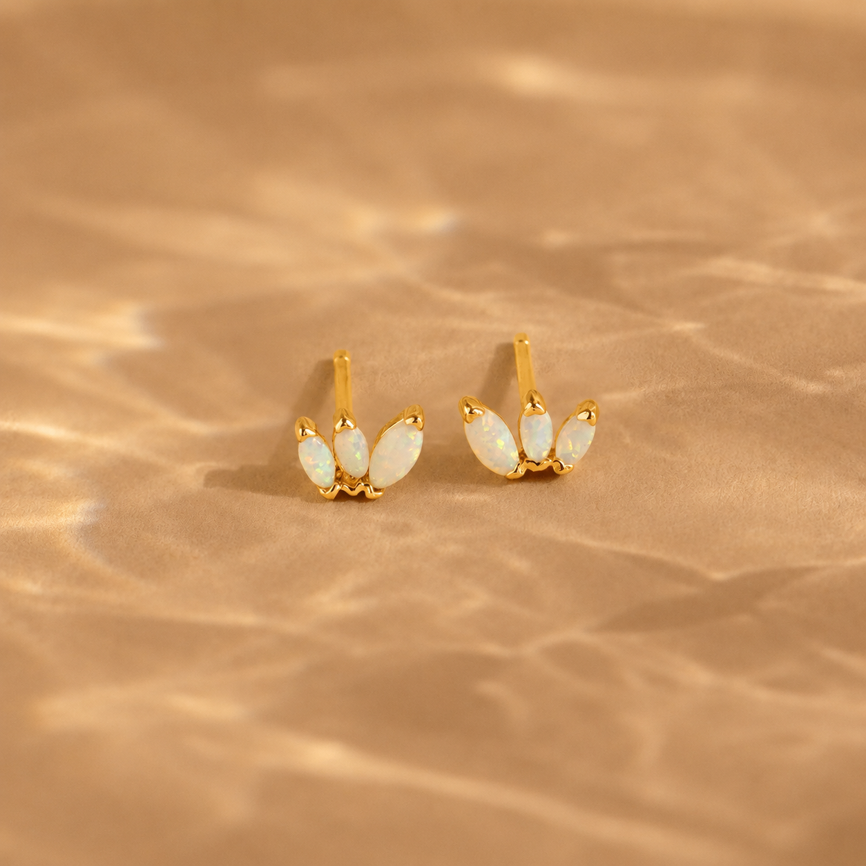Gold earrings with opal stones on a beige background