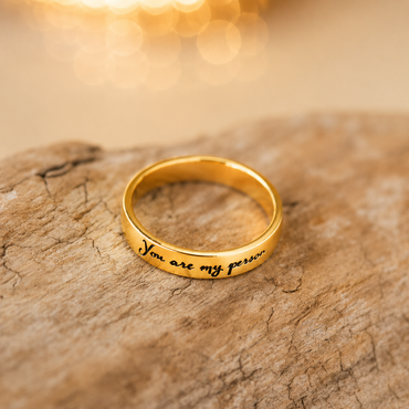 Gold ring with 'You are my person' engraving on a textured surface with a warm glow.