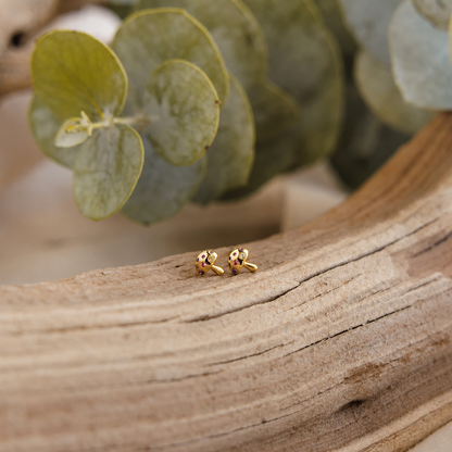 Gold earrings on a wooden surface with green leaves in the background