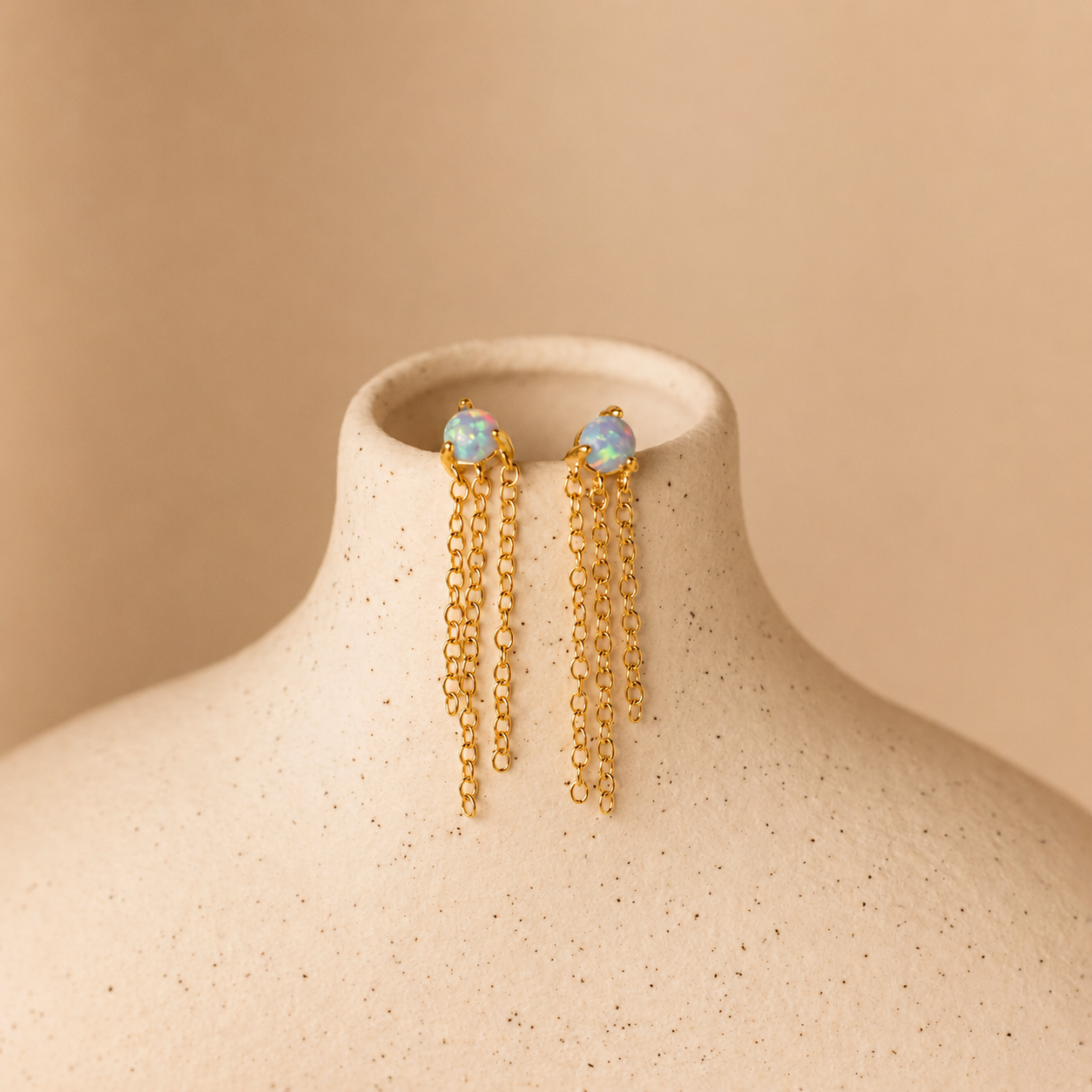 Gold earrings with opal stones on a beige mannequin bust against a beige background