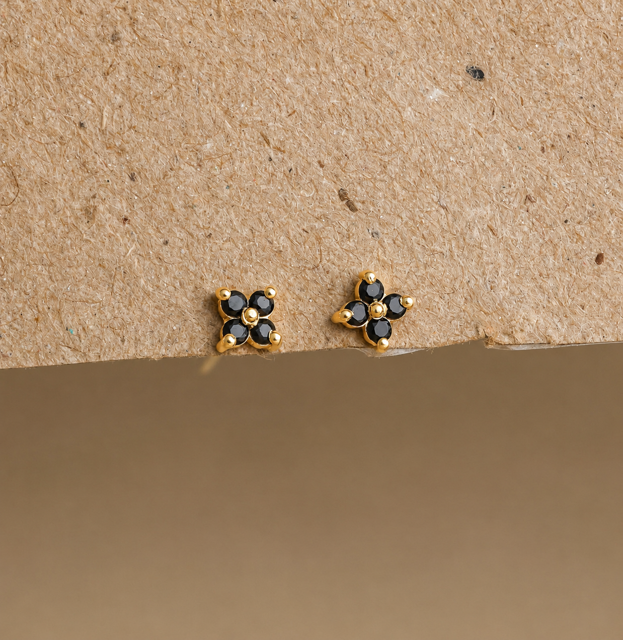 Gold and black flower-shaped earrings on a beige background