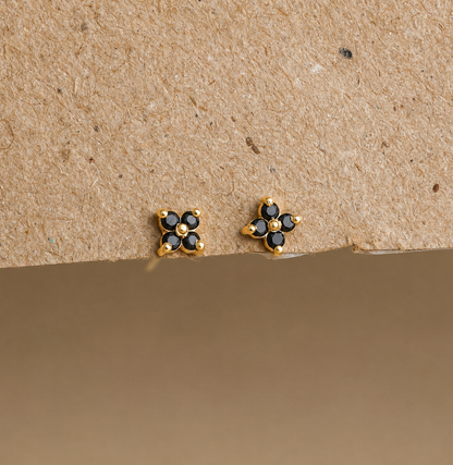 Gold and black flower-shaped earrings on a beige background