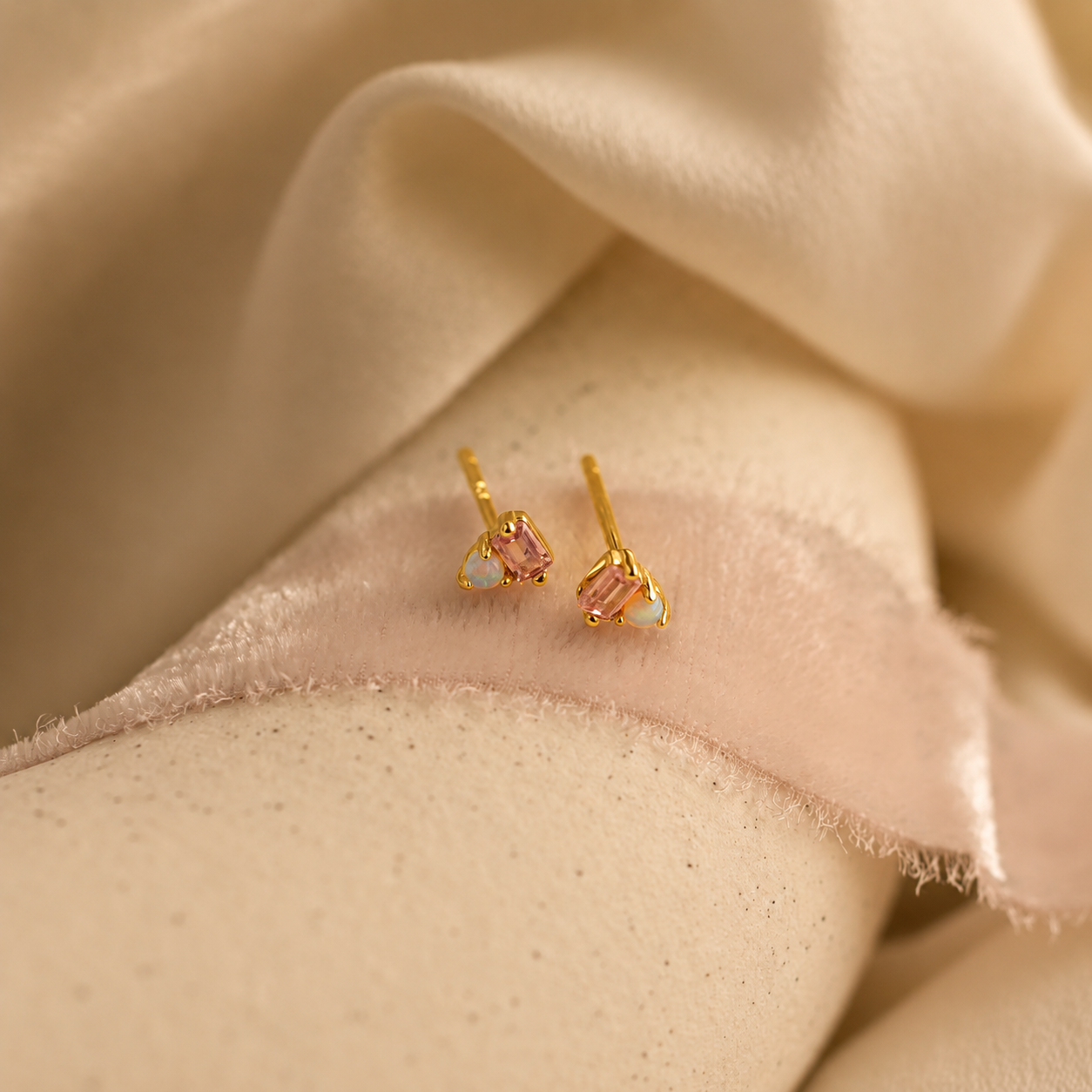 Gold earrings with pink gemstones on a beige fabric background