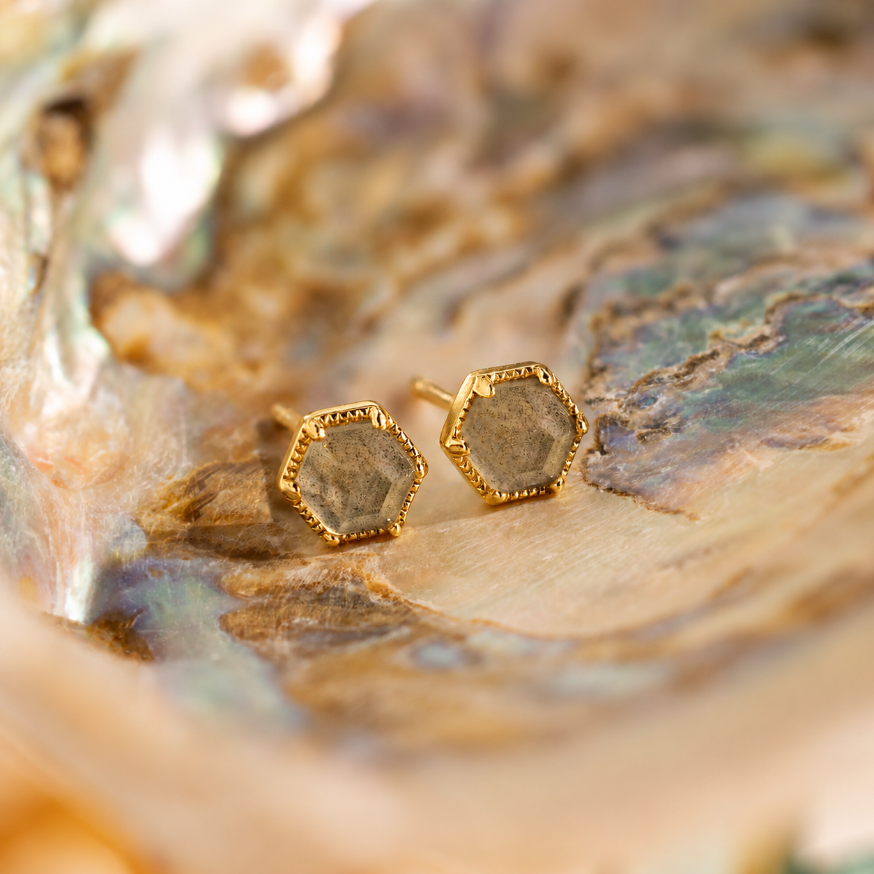Hexagonal gold earrings on a textured stone surface