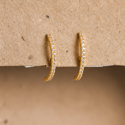 Gold hoop earrings with embedded stones on a beige background