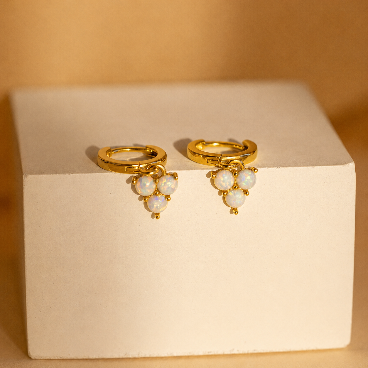Gold earrings with pearl-like stones on a beige box against a beige background