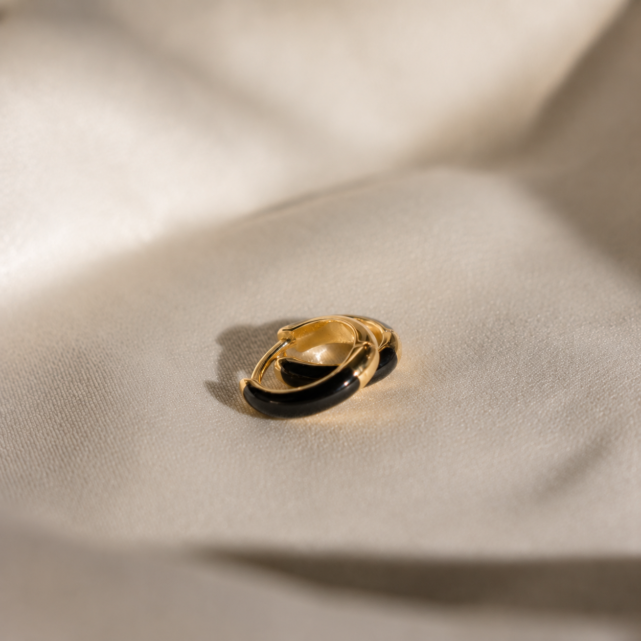 A gold ring with a curved black enamel inlay, resting on draped beige fabric with soft shadows.