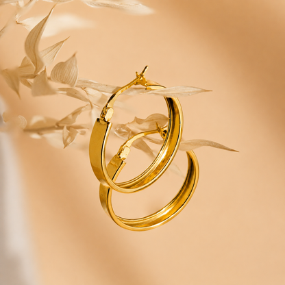 Gold hoop earrings on a beige background with leaves