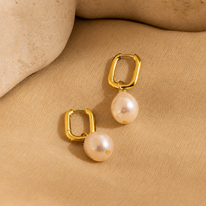 Gold hoop earrings with pearl drops on a beige fabric background