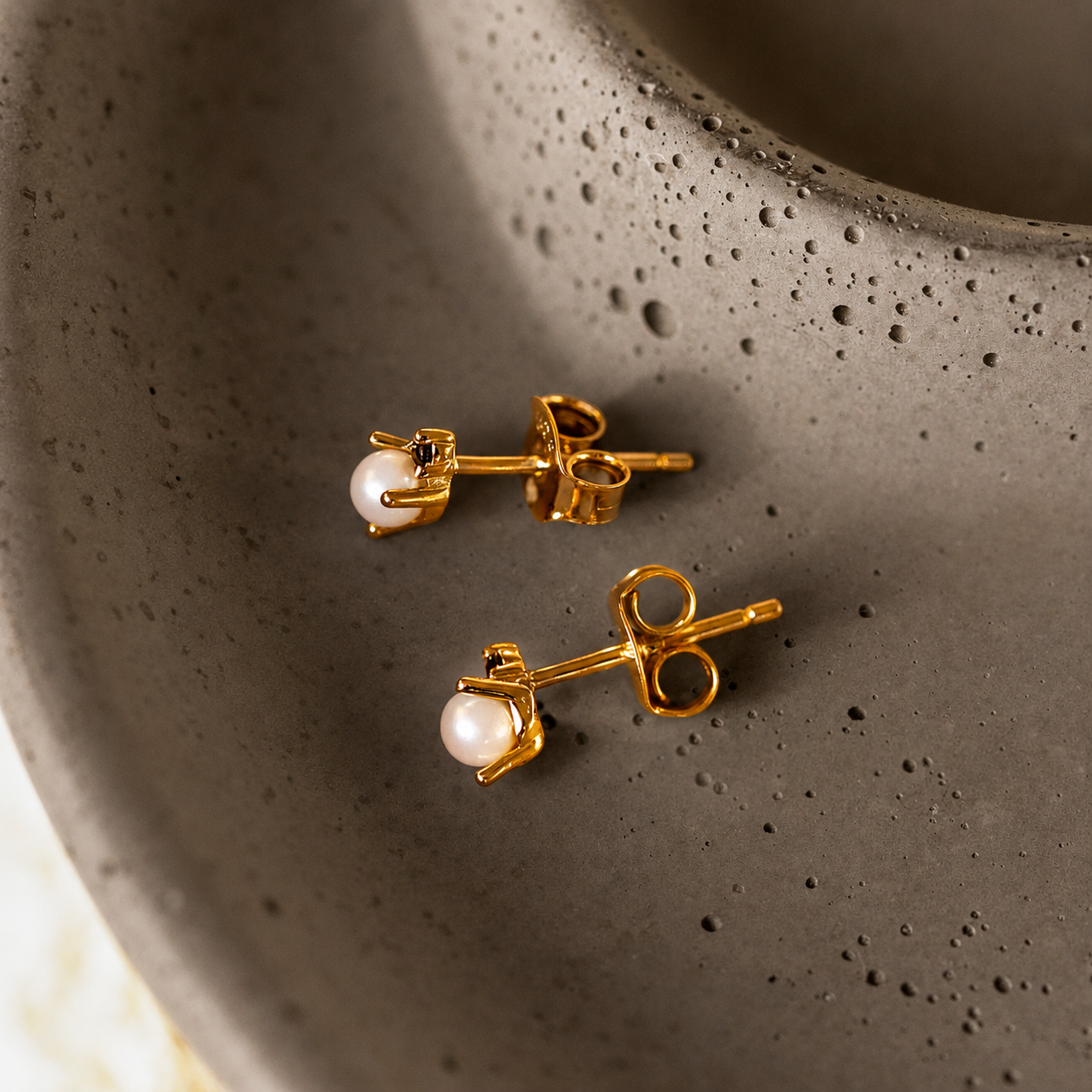 Gold earrings with pearl beads on a textured gray surface