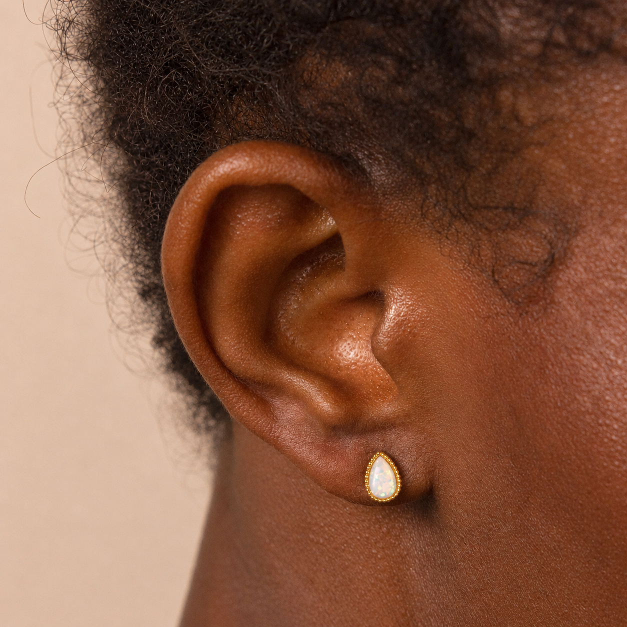Close-up of an ear wearing a gold and white teardrop earring on a beige background