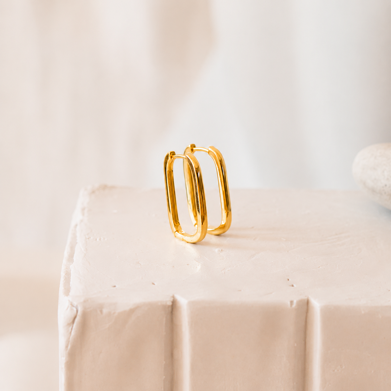 Gold hoop earrings on a beige surface with a light background
