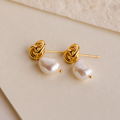 Gold earrings with pearl drops on a beige background