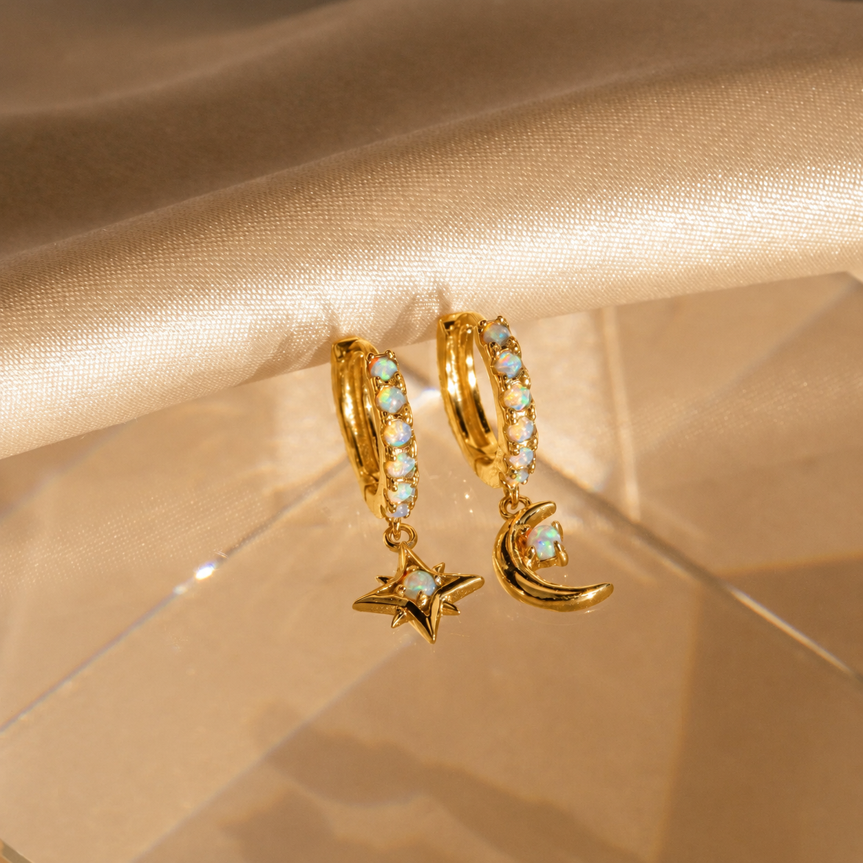 Gold hoop earrings with star and moon charms on a beige fabric background