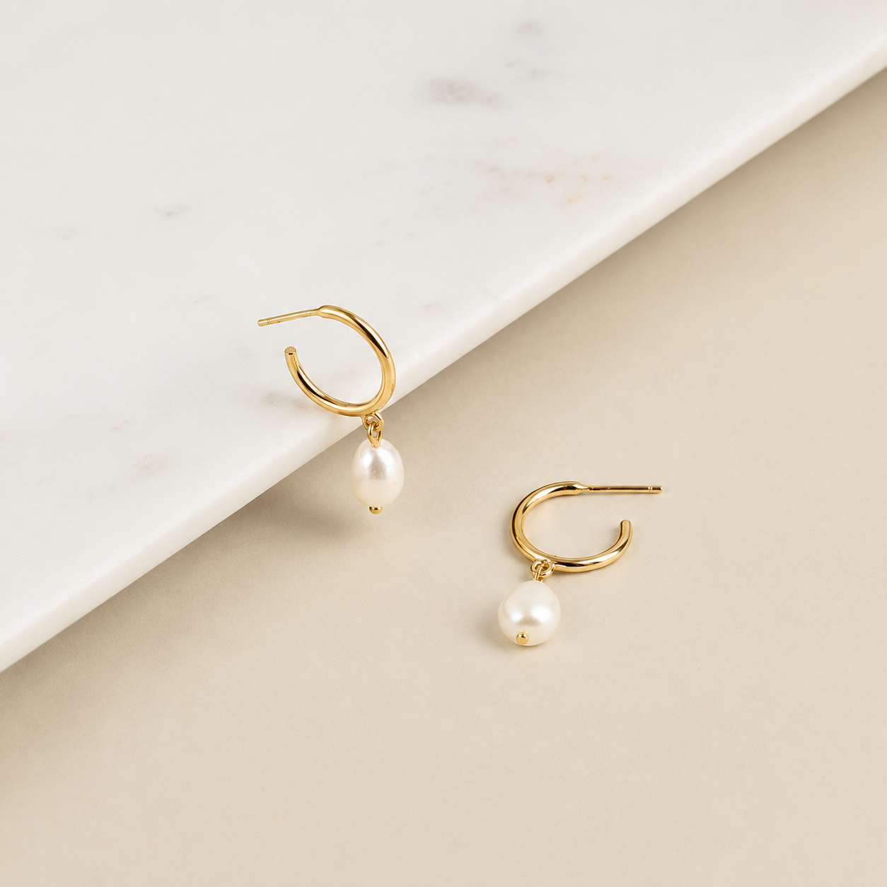 Gold hoop earrings with pearl drops on a beige and white background