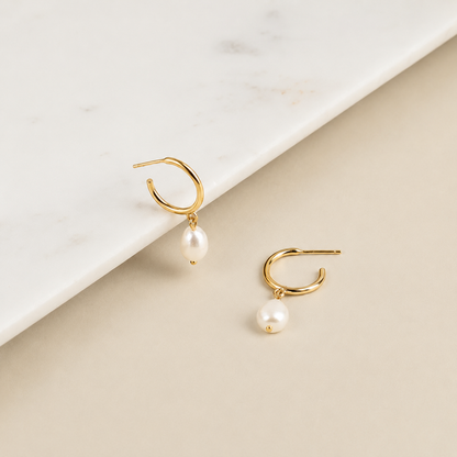 Gold hoop earrings with pearl drops on a beige and white background