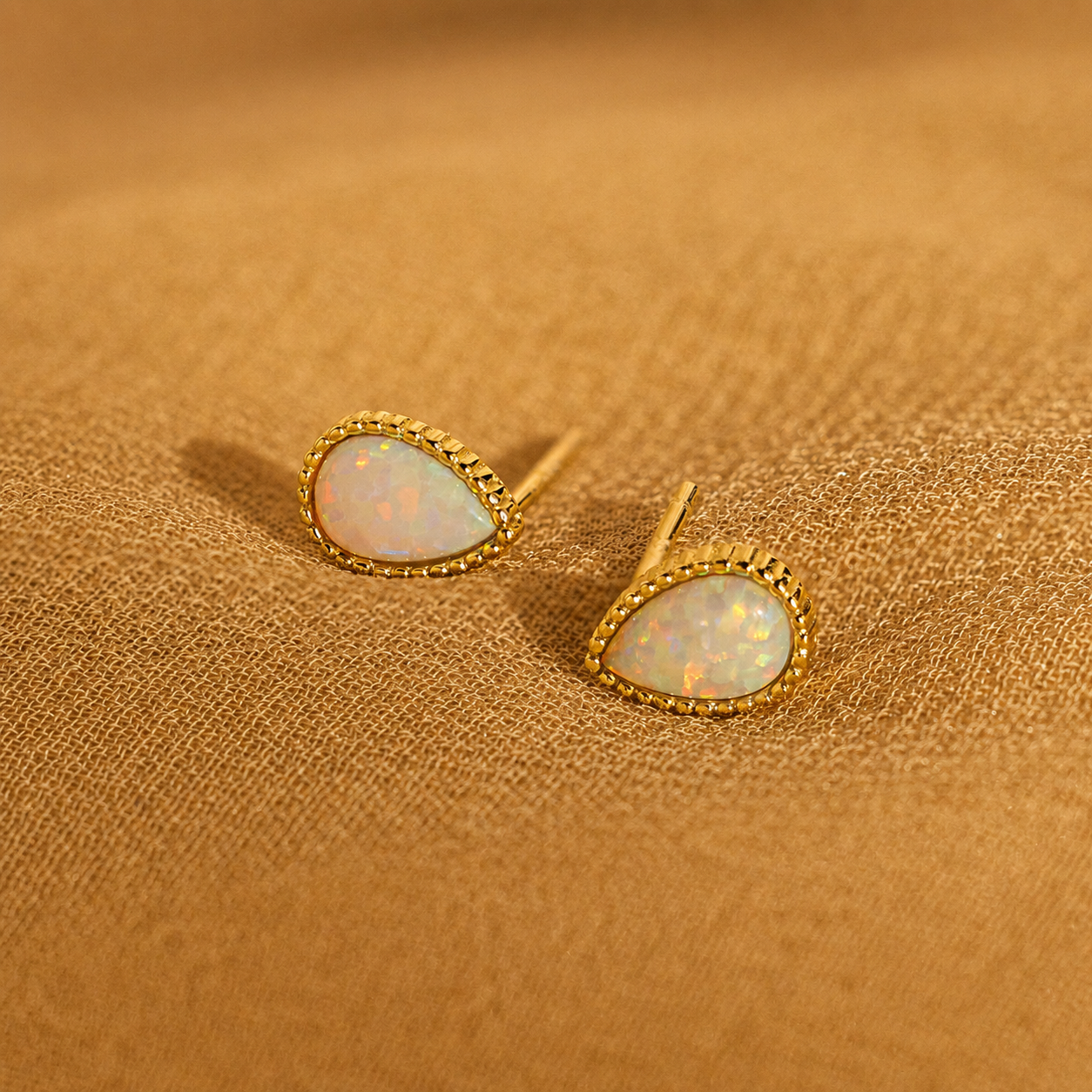 Gold earrings with opal stones on a brown fabric background