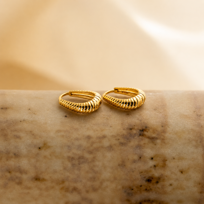 Gold hoop earrings on a textured beige surface
