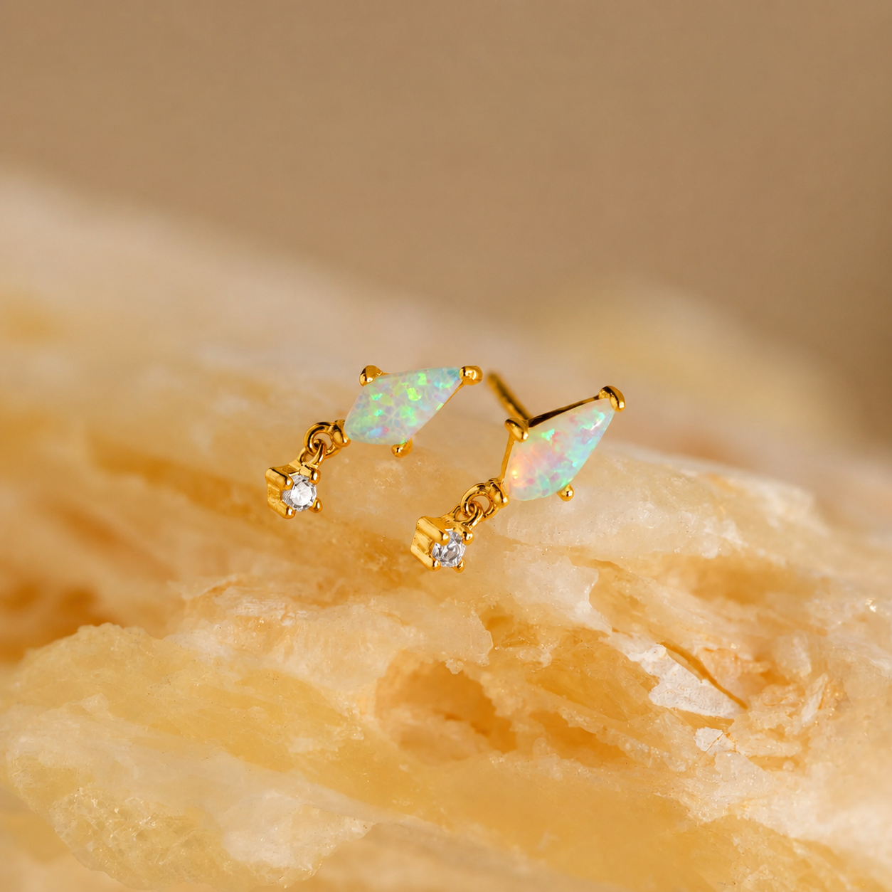 Gold earrings with opal stones on a beige stone background