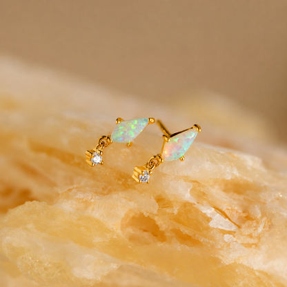 Gold earrings with opal stones on a beige stone background